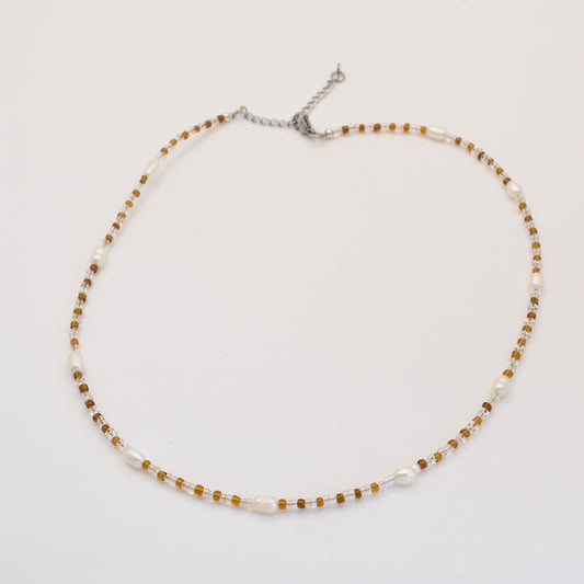 The Caramel Whispers necklace by Salty Dreamers features alternating small brown beads and white freshwater pearls on a silver adjustable chain, elegantly displayed on a plain white background.