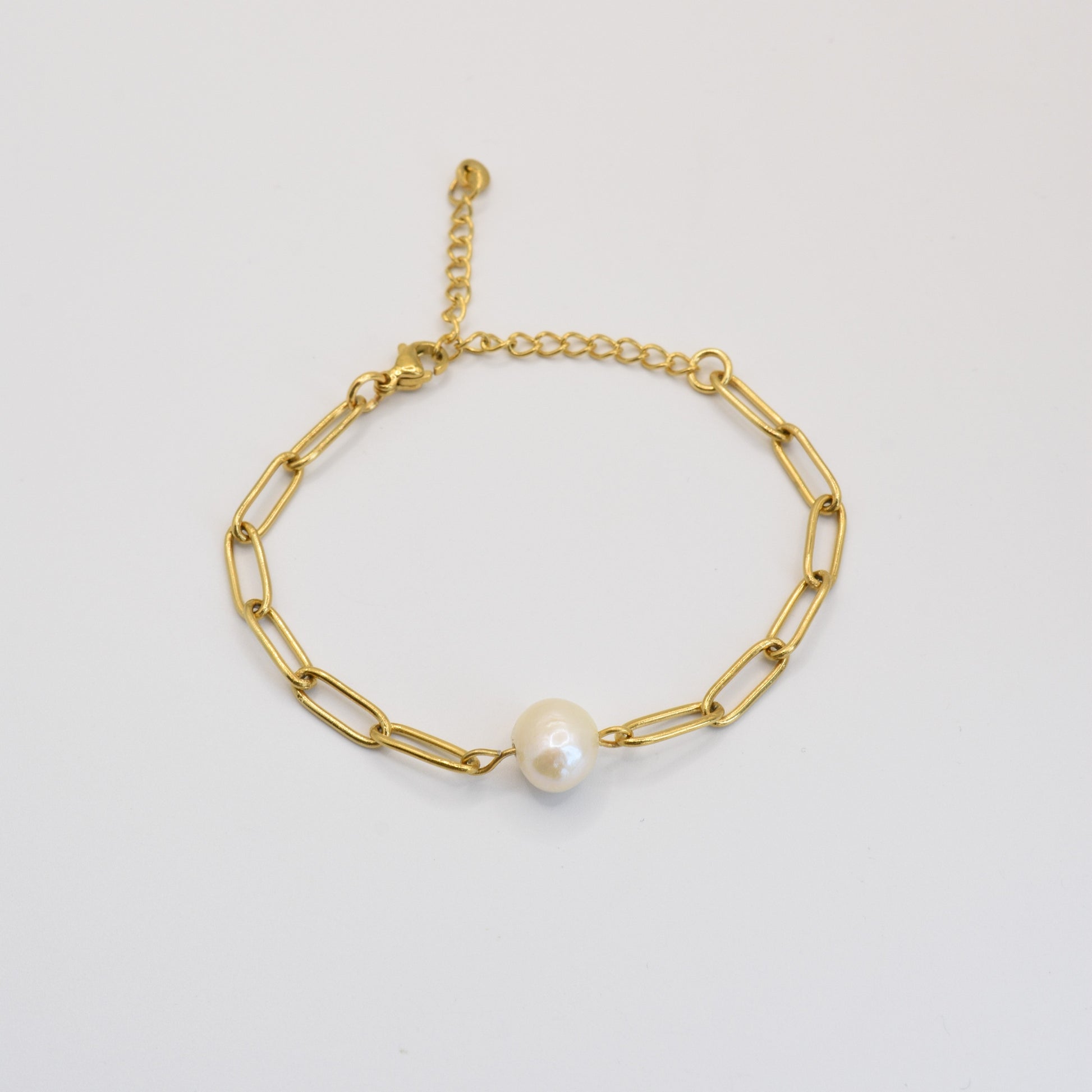 The Paperclip Cutie Gold bracelet by Salty Dreamers features elongated gold links, a single freshwater pearl centerpiece, and an adjustable clasp. This handmade piece is displayed on a plain white background.