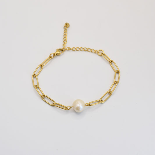 The Paperclip Cutie Gold bracelet by Salty Dreamers features elongated gold links, a single freshwater pearl centerpiece, and an adjustable clasp. This handmade piece is displayed on a plain white background.