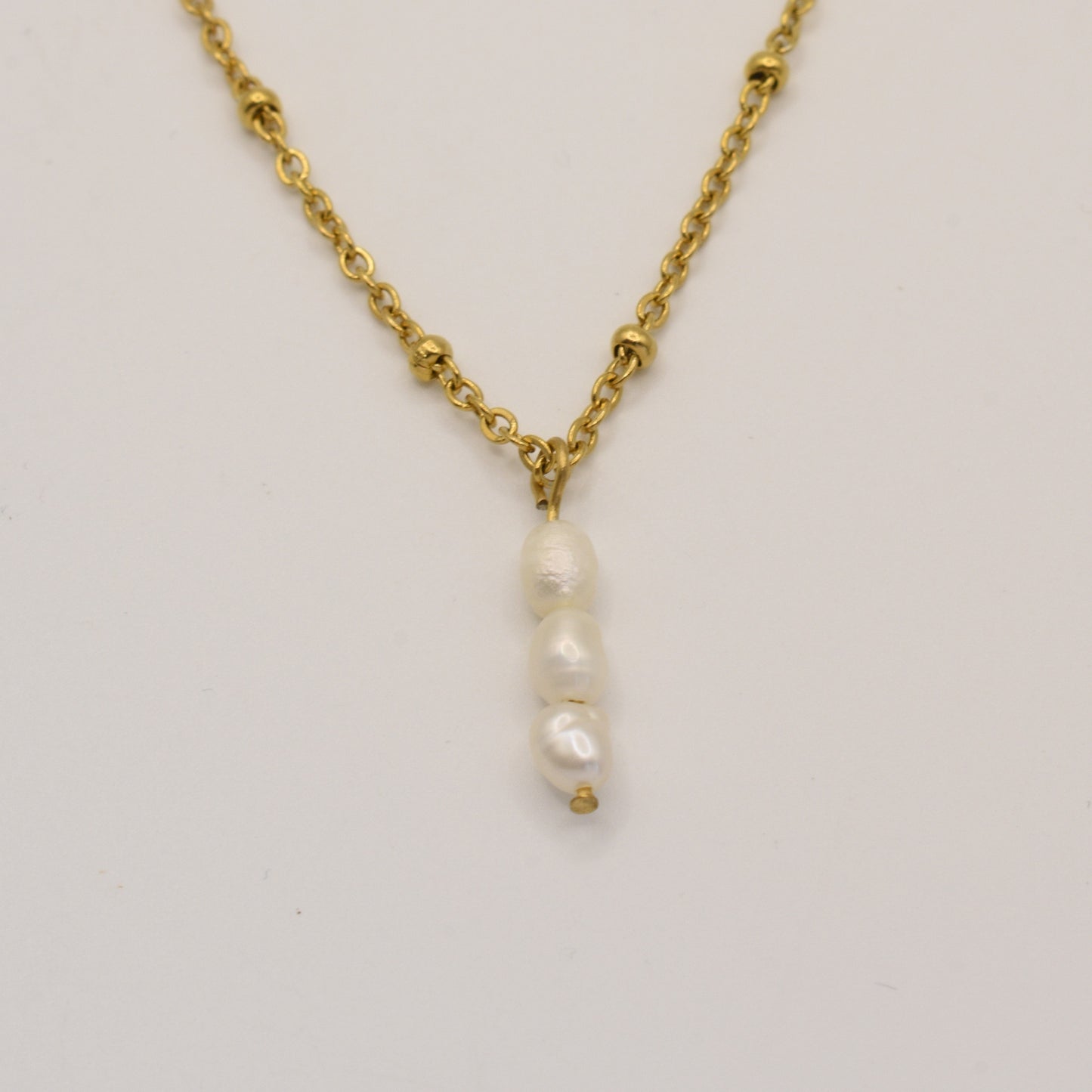 The Necklace | Cutie Pearlies by Salty Dreamers features three small, irregular freshwater pearl pendants hanging vertically on a gold chain, creating a delicate beachy style against a plain white background.