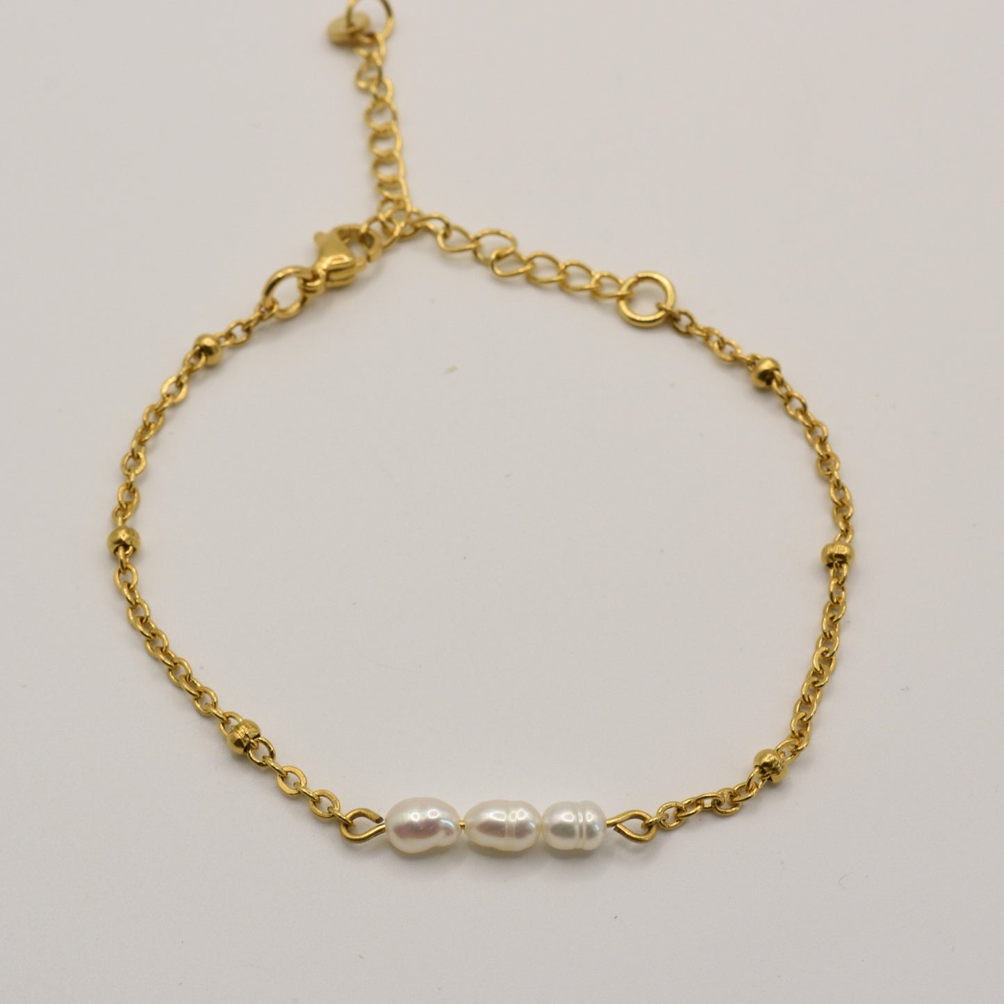 The Pretty Pearly Gold Bracelet by Salty Dreamers is a delicate handmade gold chain bracelet with three small white pearls in the center, shown on a plain white background.