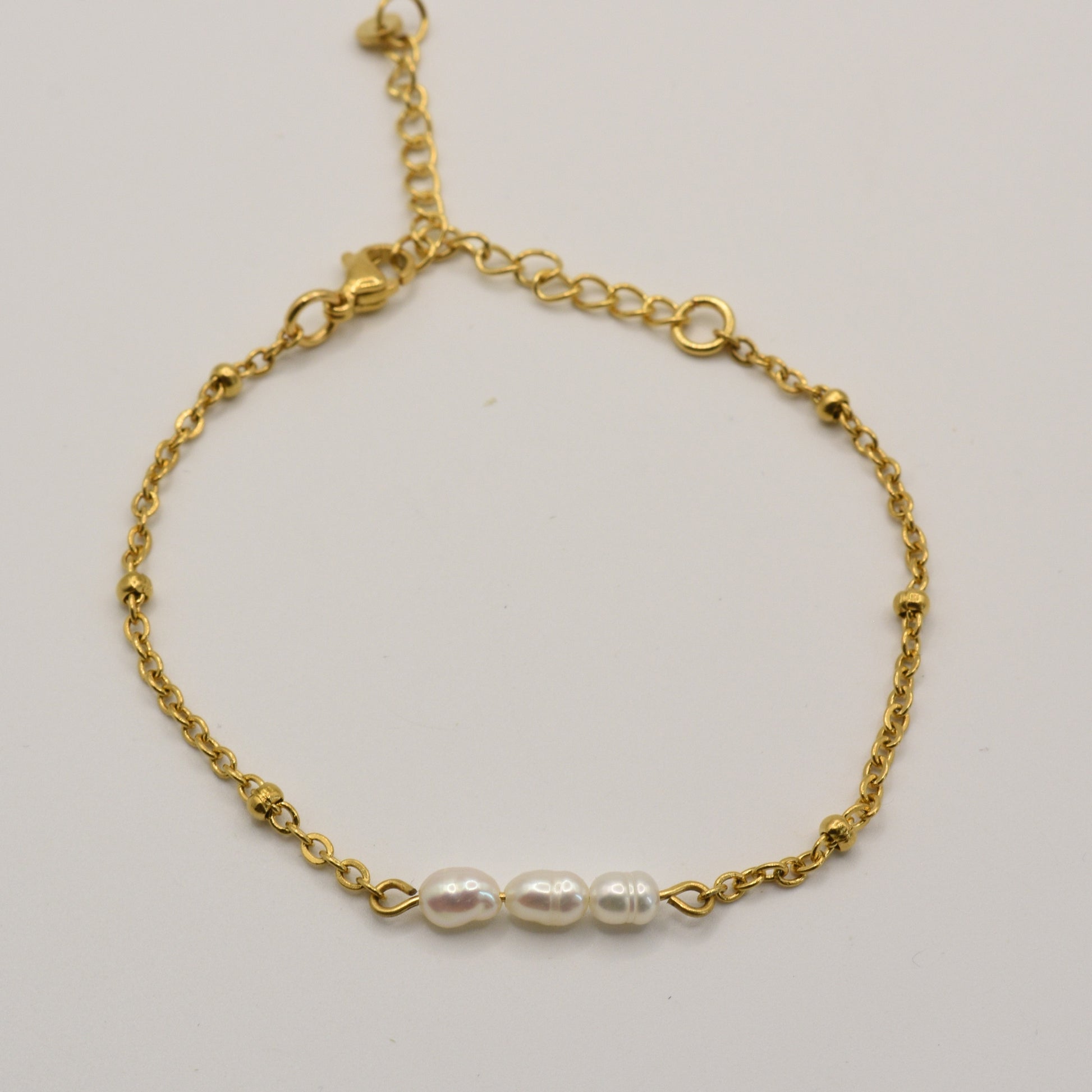 The Pretty Pearly Gold Bracelet by Salty Dreamers is a delicate handmade gold chain bracelet with three small white pearls in the center, shown on a plain white background.