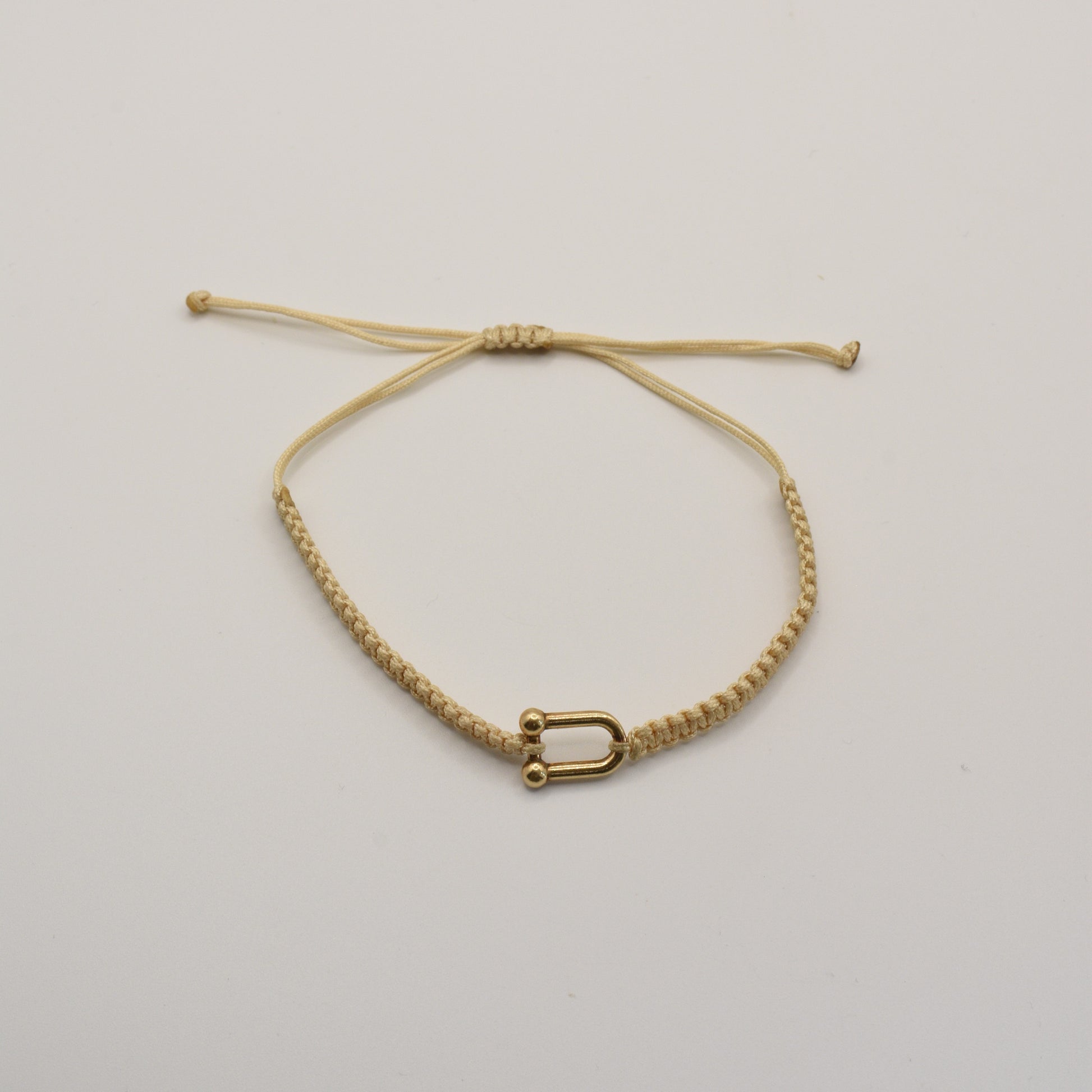 The Salty Dreamers Bracelet | Sailors Love Beige is a handmade beige macramé bracelet with a small gold-colored U-shaped charm, inspired by classic sailor shakel designs and shown on a plain white background.