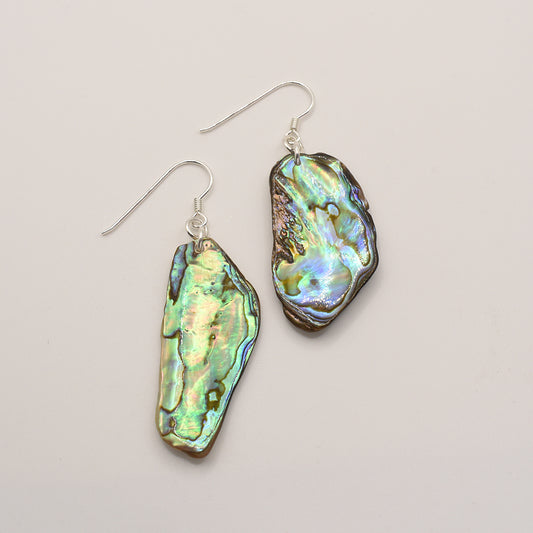 The Salty Dreamers Earrings | Paua Shell Raumati are handmade dangle earrings with large, irregular pāua shell pieces that shimmer in green, blue, and purple on a white base, finished with a silver hook.