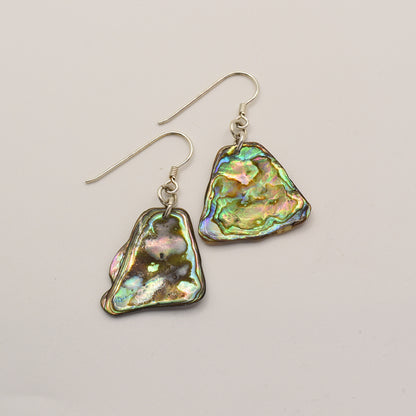 Salty Dreamers Earrings | Paua Shell Kea: Iridescent, irregularly shaped pāua shell earrings with silver hooks, displayed on a light background—a unique touch of New Zealand jewelry.