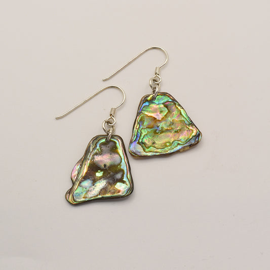 Salty Dreamers Earrings | Paua Shell Kea: Iridescent, irregularly shaped pāua shell earrings with silver hooks, displayed on a light background—a unique touch of New Zealand jewelry.
