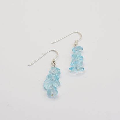 The Glassy Spring earrings by Salty Dreamers feature clusters of irregular, translucent blue glass stones and 925 silver hooks, displayed vertically on a plain white background.