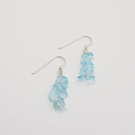 The Glassy Spring earrings by Salty Dreamers feature clusters of irregular, translucent blue glass stones and 925 silver hooks, displayed vertically on a plain white background.