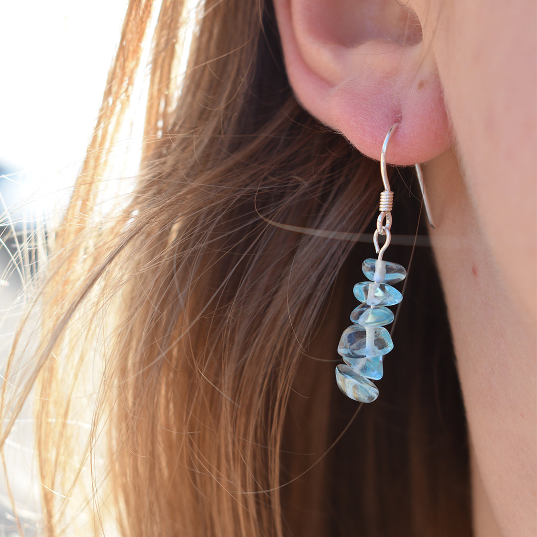Close-up of a person wearing Salty Dreamers’ Glassy Spring earrings. The 925 silver handmade earrings feature stacked, irregular blue-green gemstone beads, elegantly framed by light brown hair.