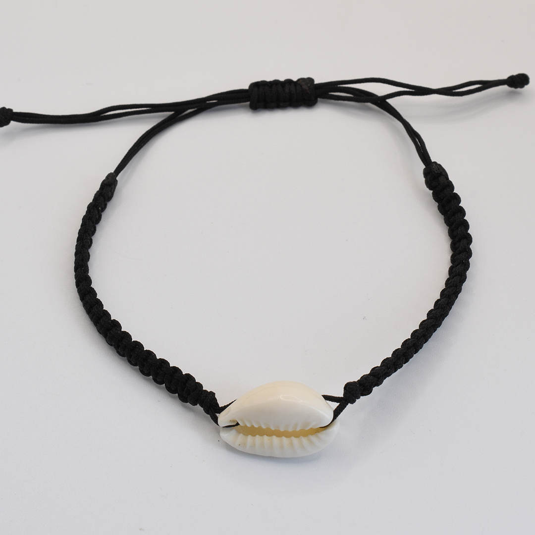 The Salty Dreamers Bracelet | Macramazing Cowrie Black features a black braided macrame design with a white cowrie shell centerpiece and an adjustable fit, shown on a plain white background.