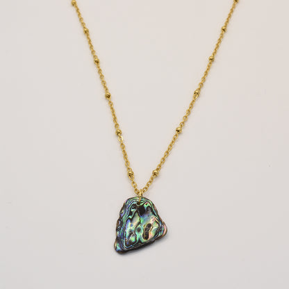 The Salty Dreamers Necklace | Paua Shell Moana features a gold chain with small beads and an iridescent triangular pāua shell pendant, inspired by New Zealand jewelry traditions. Shown on a plain white background.