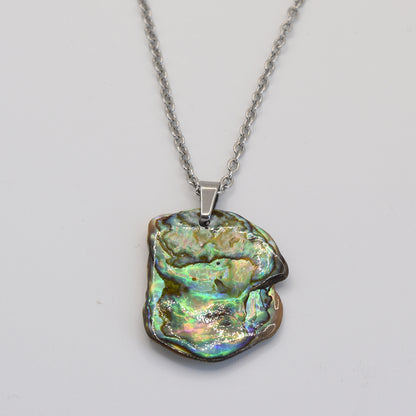 The Salty Dreamers Necklace | Paua Shell Kaukau features a handmade silver chain with an irregular paua shell pendant, showcasing shimmering green, blue, and gold hues against a white background.