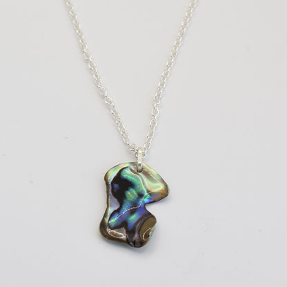 The Salty Dreamers Necklace | Paua Shell Kea features a handmade silver pendant with an irregular pāua shell, showcasing shimmering green, blue, and purple hues on white.
