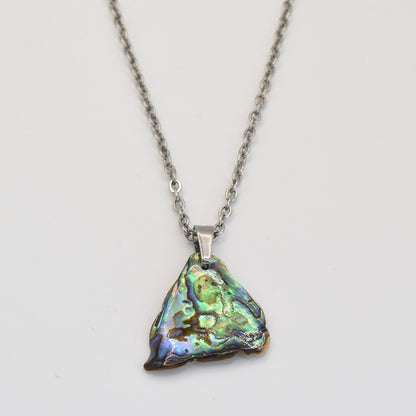 The Salty Dreamers Paua Shell Ngaru necklace features a handmade silver chain and a triangular, iridescent abalone pendant with green, blue, and gold hues, shown on a white background.