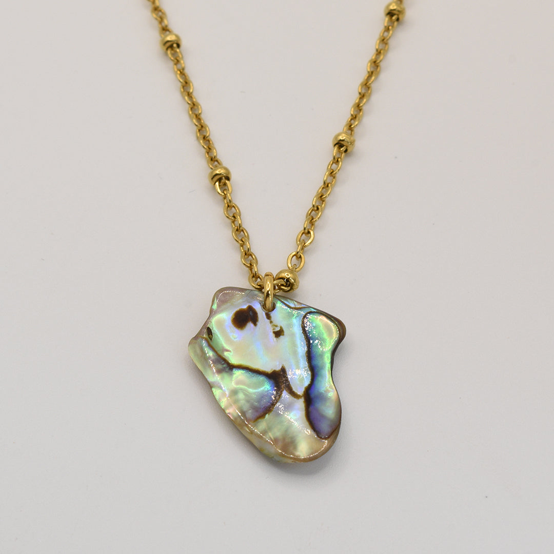 The Salty Dreamers Necklace | Paua Shell Kiri features a gold chain with an irregular, iridescent New Zealand paua shell pendant displayed on a plain white background.