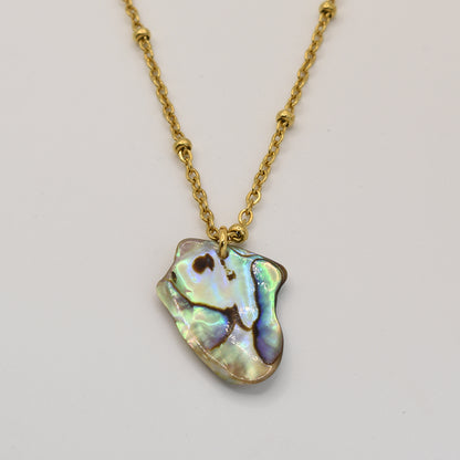The Salty Dreamers Necklace | Paua Shell Kiri features a gold chain with an irregular, iridescent New Zealand paua shell pendant displayed on a plain white background.