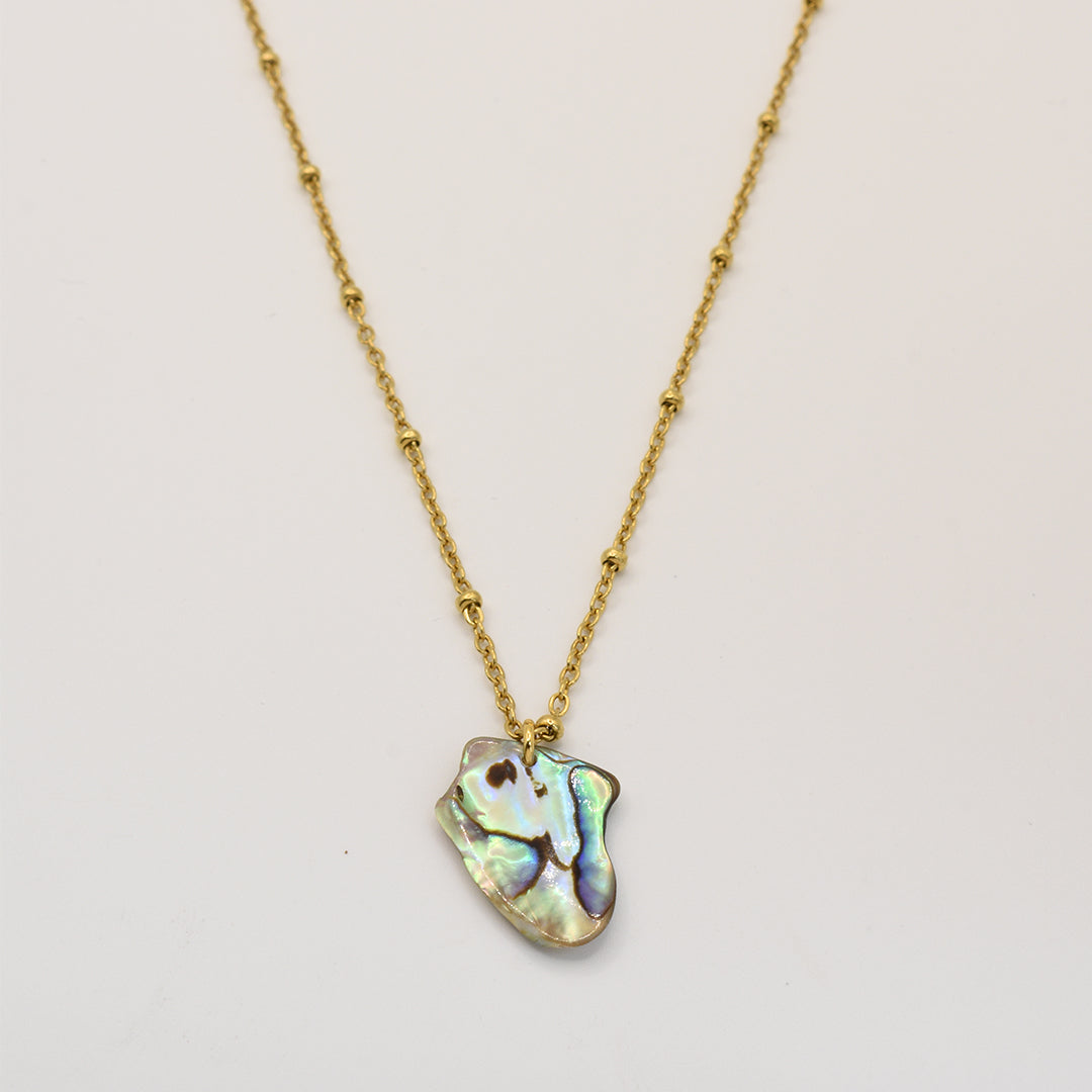 The Salty Dreamers Necklace | Paua Shell Kiri is a gold chain with small decorative beads and an iridescent, irregular New Zealand abalone shell pendant, shown on a plain white background.