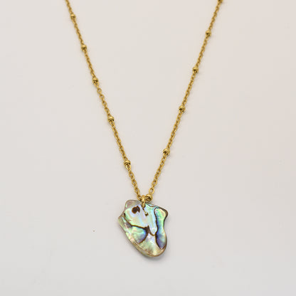 The Salty Dreamers Necklace | Paua Shell Kiri is a gold chain with small decorative beads and an iridescent, irregular New Zealand abalone shell pendant, shown on a plain white background.