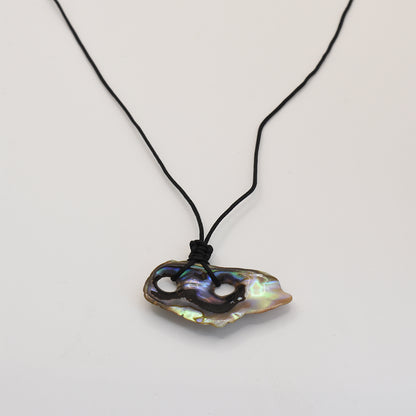 The Salty Dreamers Necklace | Paua Shell Haeata features a handmade black cord and an iridescent, irregularly shaped pāua shell pendant with two carved holes—an elegant New Zealand jewelry piece displayed on white.