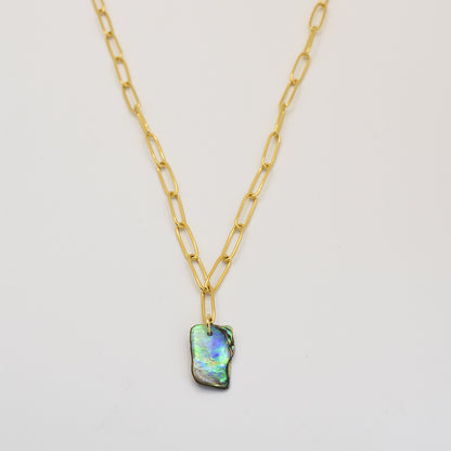 The Paua Shell Tautahi Necklace by Salty Dreamers features a gold paperclip chain and a rectangular iridescent abalone pendant, highlighting handmade beauty against a white background.
