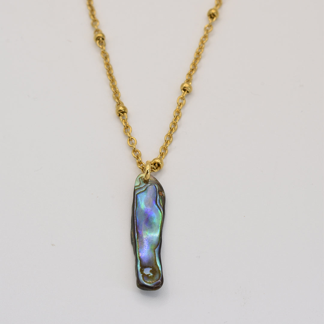 The Salty Dreamers Necklace | Paua Shell Ra features a gold chain with small round beads and a rectangular iridescent pāua shell pendant, showcasing elegant New Zealand jewelry against a white background.