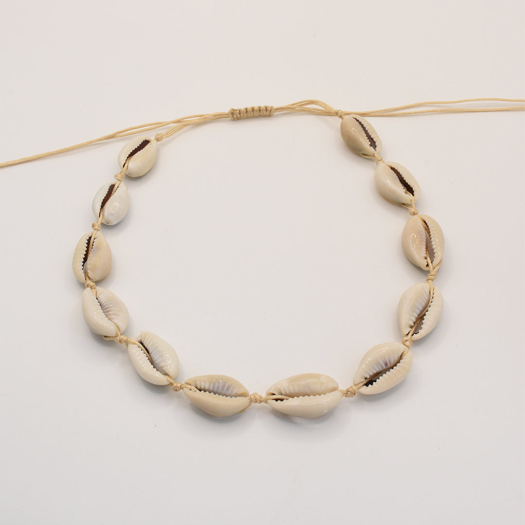 The Salty Dreamers Necklace | Cowrie Choker features seven handmade white cowrie shells on a beige cord, evenly spaced and shown on a plain white background. Ideal as subtle beach jewelry.
