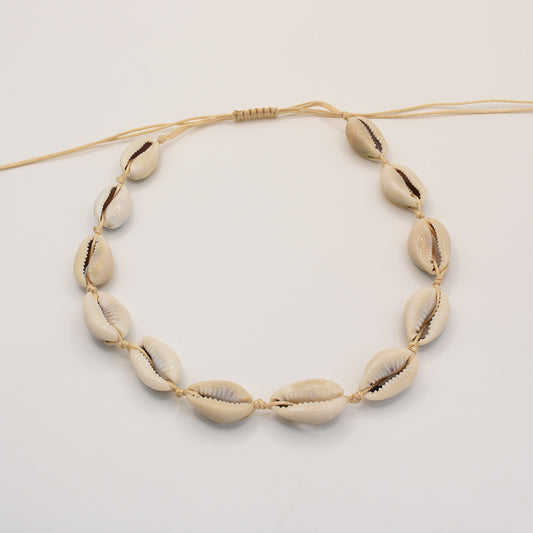 The Salty Dreamers Necklace | Cowrie Choker features seven handmade white cowrie shells on a beige cord, evenly spaced and shown on a plain white background. Ideal as subtle beach jewelry.