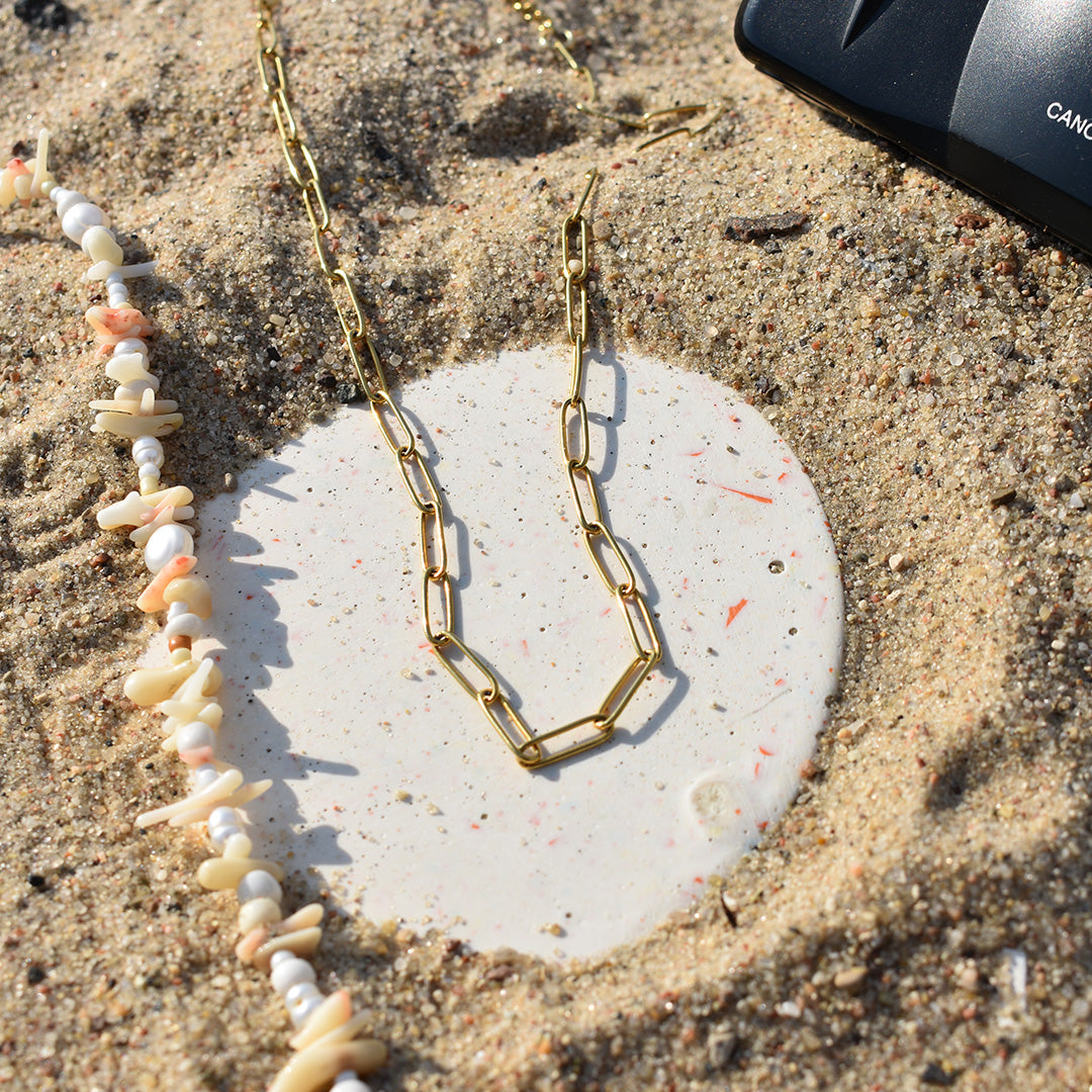 The Necklace | Golden Vibes by Salty Dreamers is a handmade gold chain necklace, shown on a white stone with sand and seashells—ideal for anyone who loves surfer jewelry style.