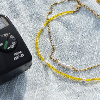 The Salty Dreamers Necklace | Starfish, featuring colorful handmade beads and small pearls, is displayed on light blue textured fabric beside the corner of a black electronic device.