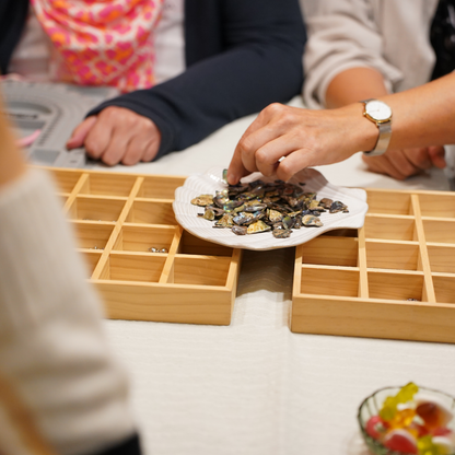 At the Salty Dreamers Workshop Ocean Jewellery in Kiel, participants casually sort polished stones on a white plate, with wooden trays on the table as they prepare to craft their own unique jewelry creations.