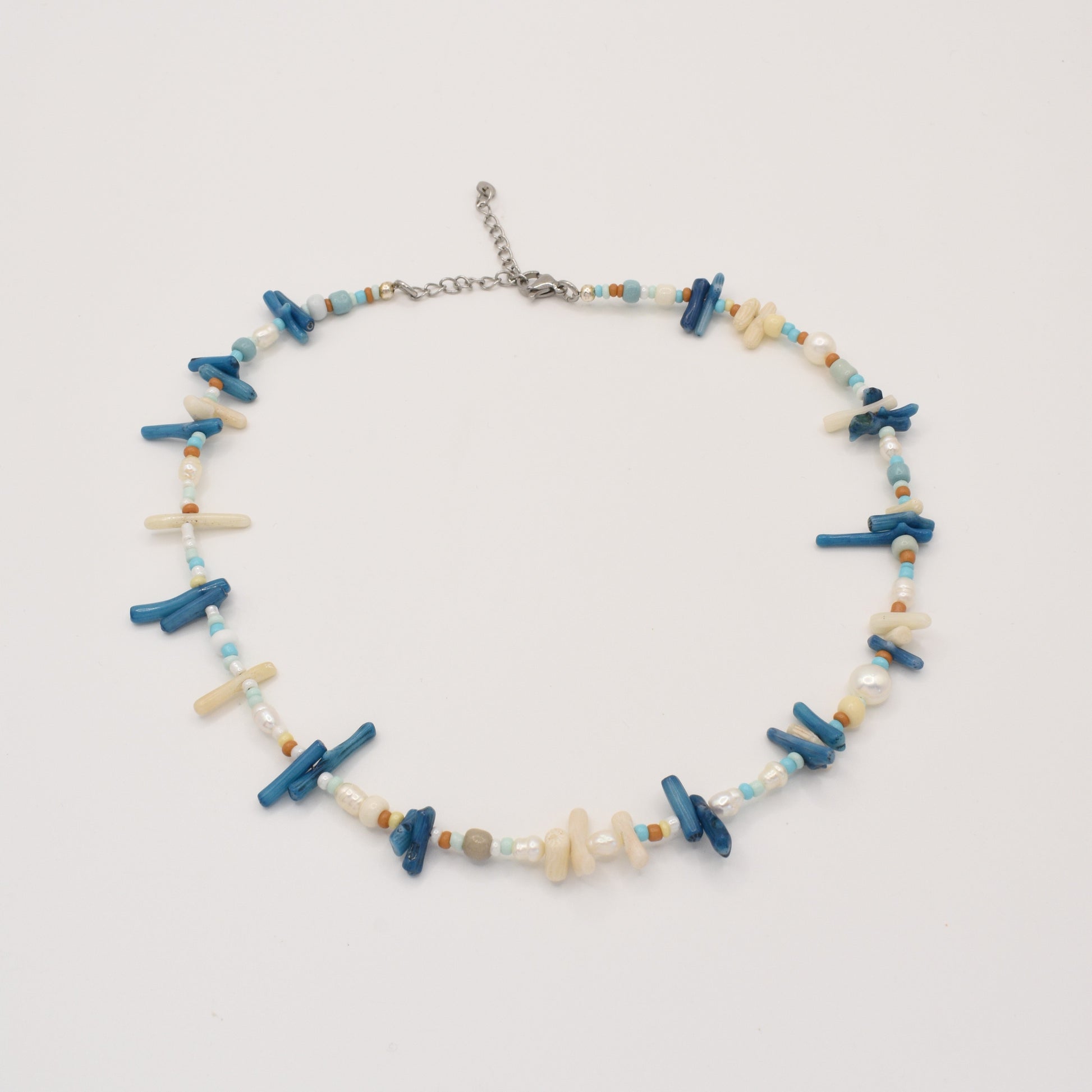 The Salty Dreamers Necklace | Ocean Bamboo Blue is a handmade piece with irregular blue and cream stick beads, turquoise and brown rounds, and white pearls, finished with a silver adjustable clasp. Displayed on a white background.