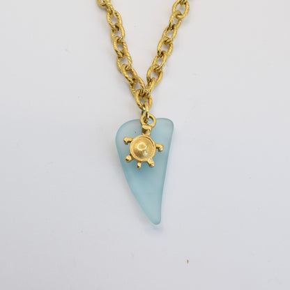 The Salty Dreamers Necklace | Turtle Sea Glass features a golden chain with a light blue, teardrop-shaped seaglass stone and a small gold sunburst accent, capturing the essence of ocean beauty.