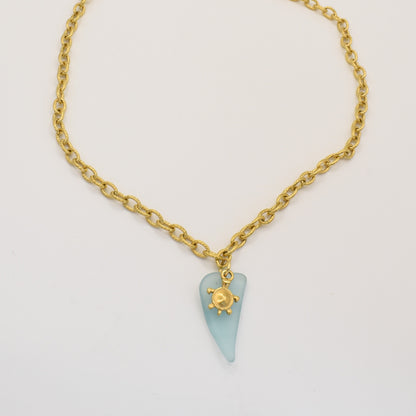 The Salty Dreamers Necklace | Turtle Sea Glass features a blue sea glass pendant with a gold turtle charm, beautifully showcased on a white background.