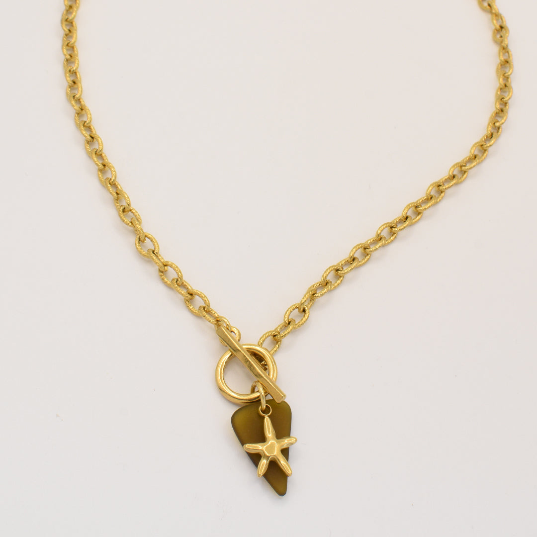 The Salty Dreamers Star Sea Glass necklace is handmade with a genuine brown sea glass pendant, a small gold starfish charm, and a golden stainless steel toggle clasp, beautifully displayed on a plain white background.