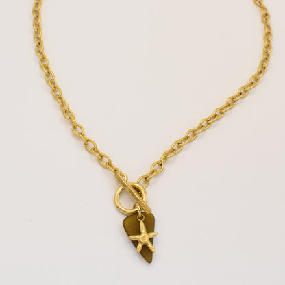 The Salty Dreamers Star Sea Glass necklace is handmade with a genuine brown sea glass pendant, a small gold starfish charm, and a golden stainless steel toggle clasp, beautifully displayed on a plain white background.