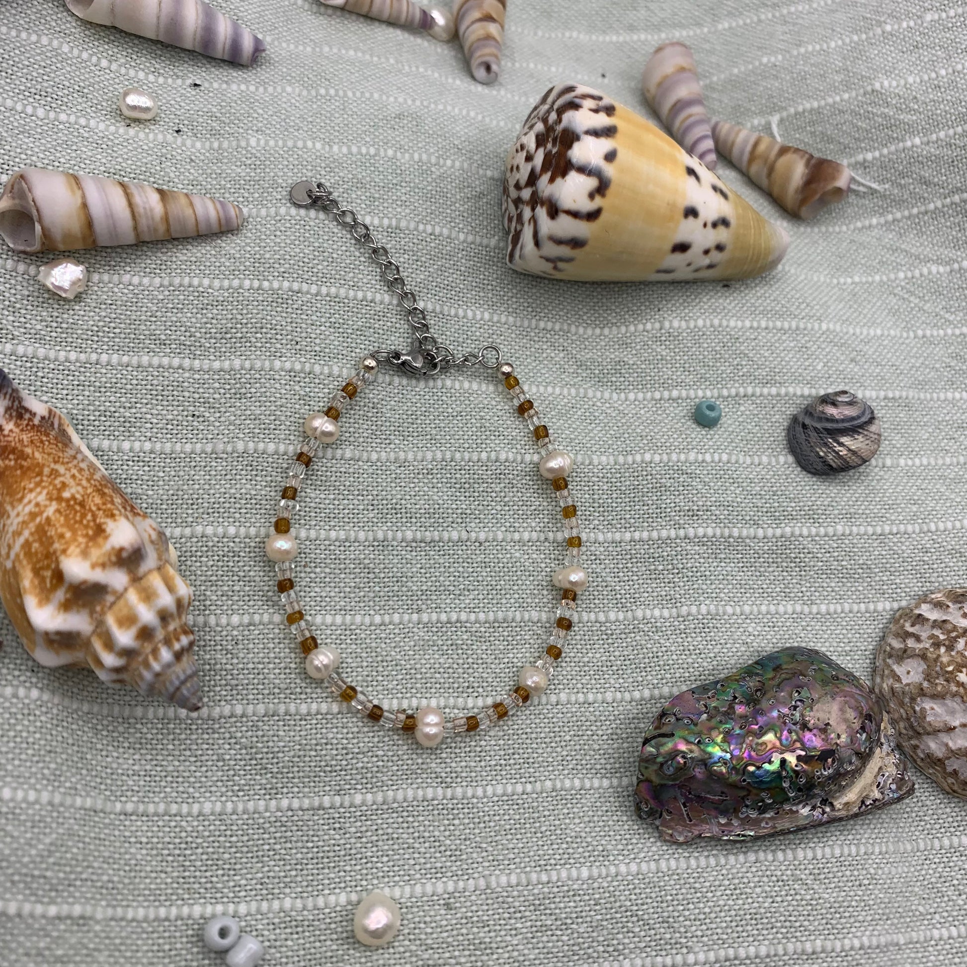 Necklace with pearls and beads surrounded by seashells on a textured fabric background